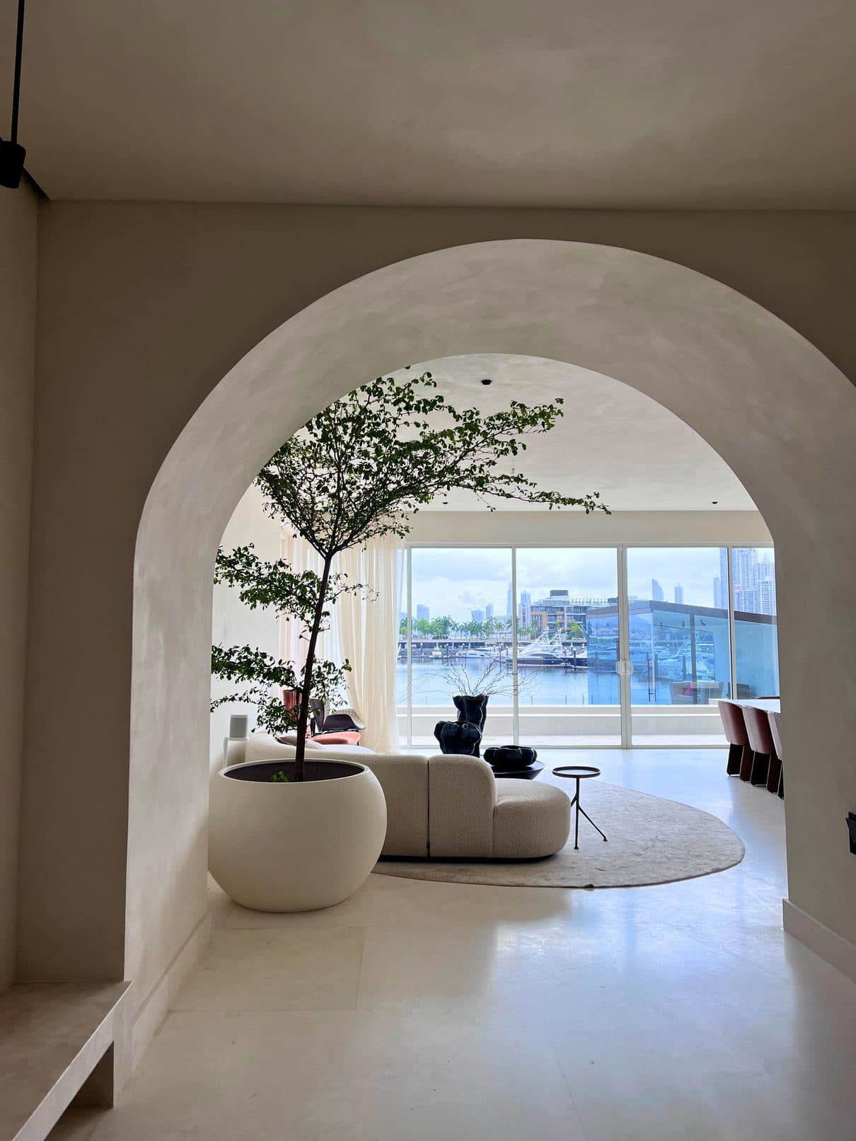 Árbol de interior en maceta blanca bajo un arco, en una sala frente al mar